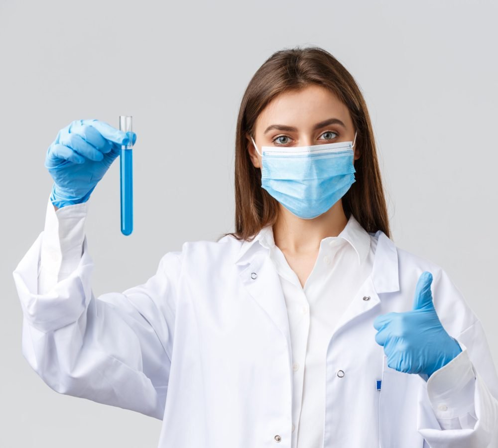 Covid-19, preventing virus, healthcare workers and quarantine concept. Doctor finished coronavirus vaccine test, holding test-tube with sample and approve it, thumbs-up guarantee quality.